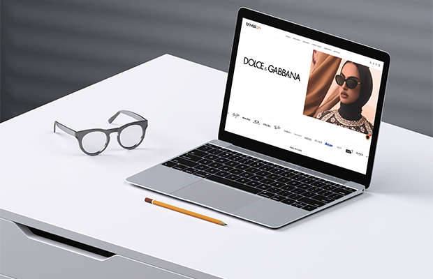 Trivision optical e-commerce website mockup on a laptop showing Dolce & Gabbana eyewear collection on a clean white desk