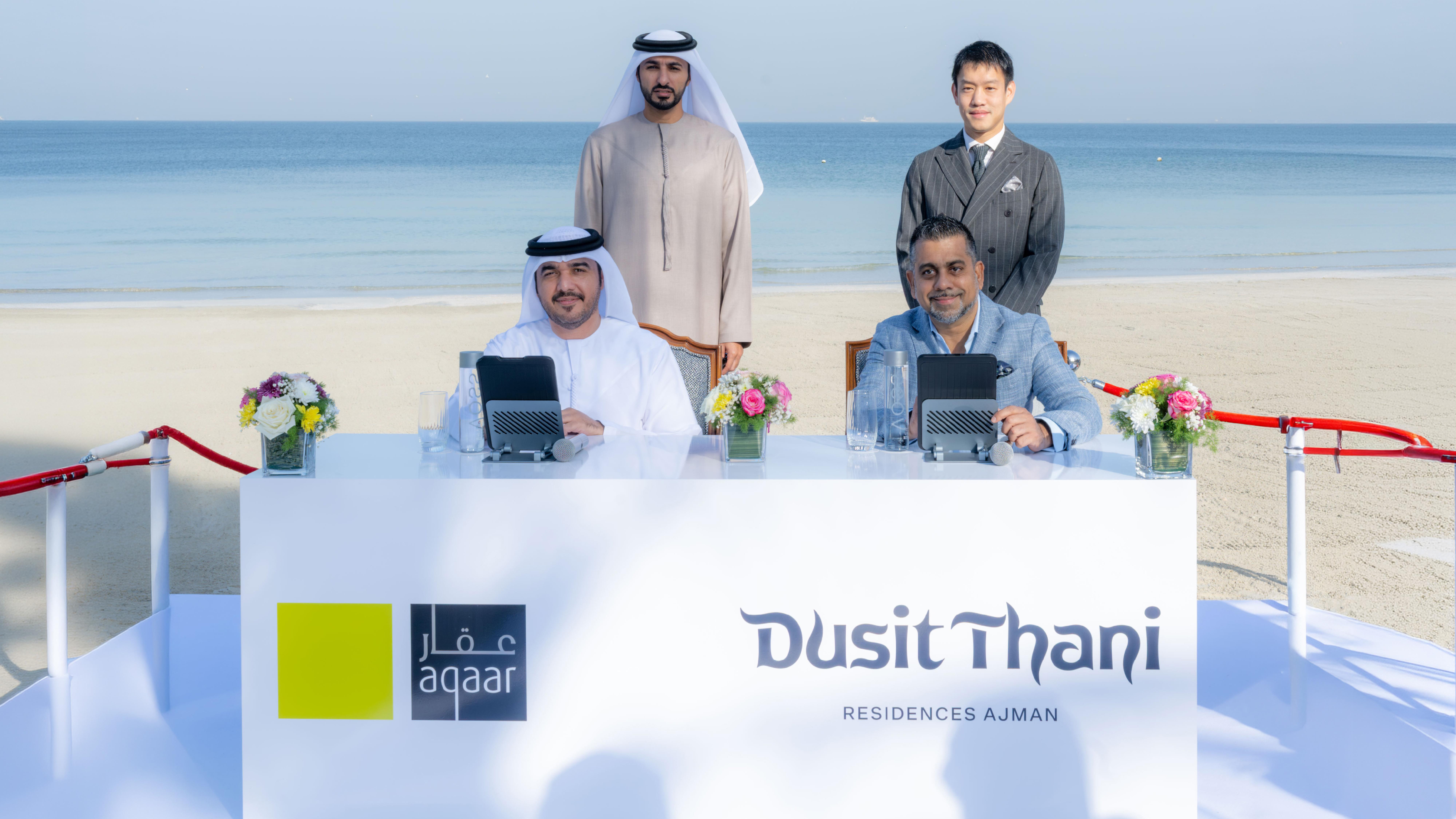 Executives and representatives posing at a beachfront signing ceremony for Aqaar and Dusit Thani Residences Ajman partnership.