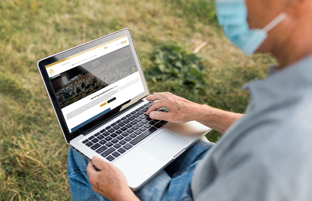 Person wearing a face mask browsing the SMASIM website on a laptop while sitting outdoors on grass